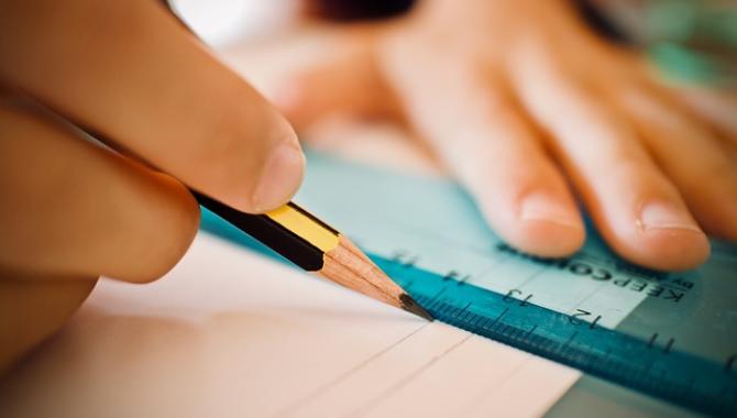 student drawing a line using pencil and ruler