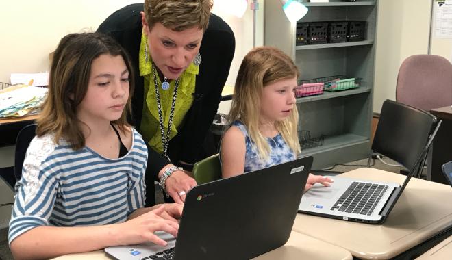 teacher helping students on laptops