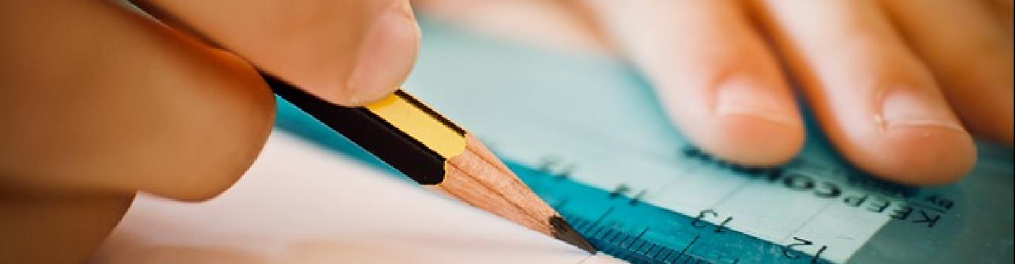 student drawing a line using pencil and ruler